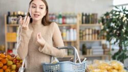 A woman with a shopping basket in a supermarket uses her smartphone with voice commands to assist her shopping.